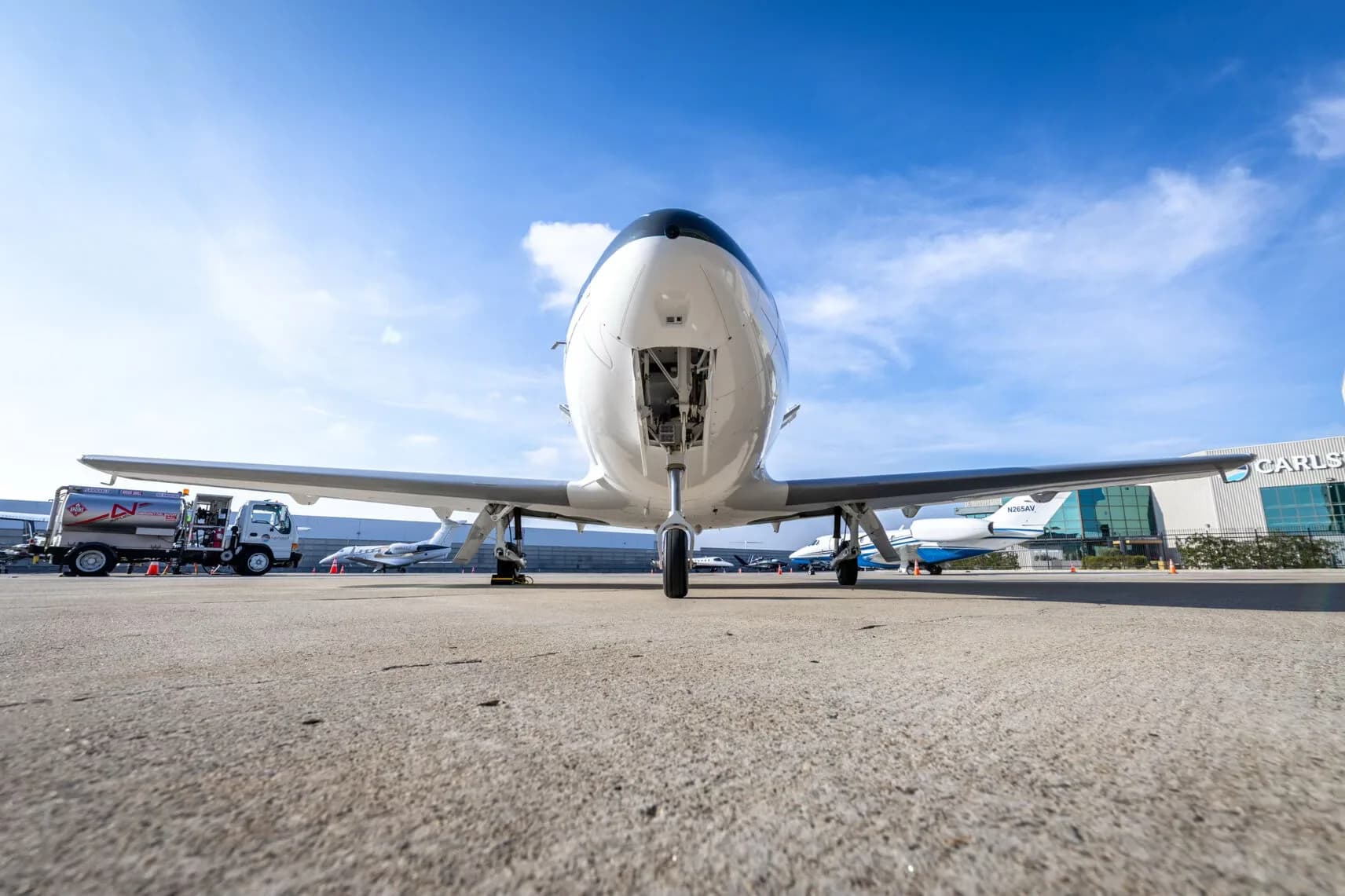 A low-angle front view of a white and dark grey Cirrus Vision Jet (N82WF) with its nose landing gear extended on an airport tarmac.