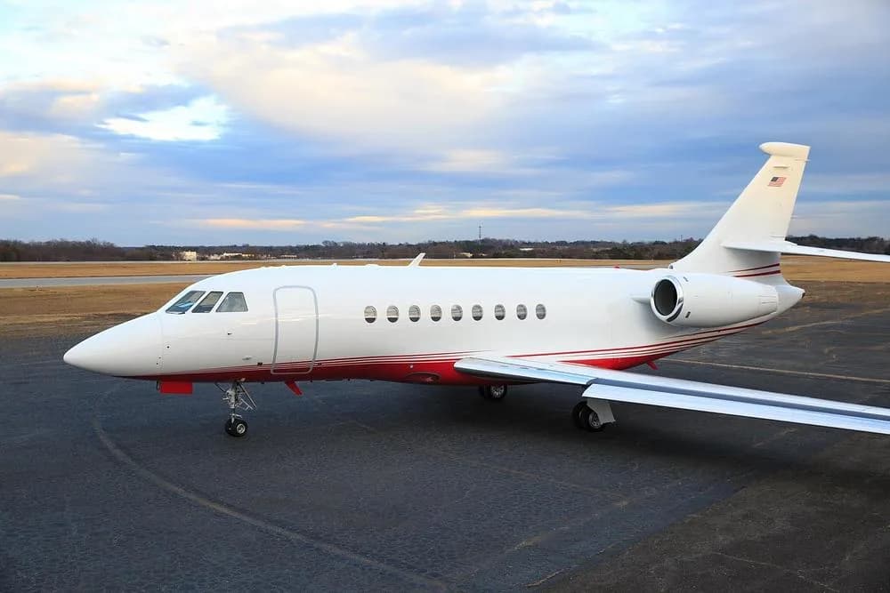 A side view of a white and red Dassault Falcon 900 private jet parked on an airport tarmac.