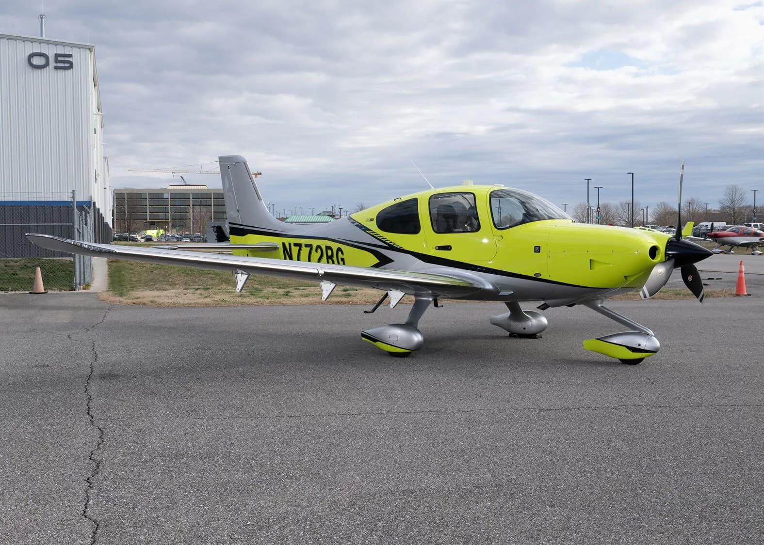 A three-quarter front view of the yellow and silver Cirrus SR22, N772RG, parked on an airfield next to a hangar.