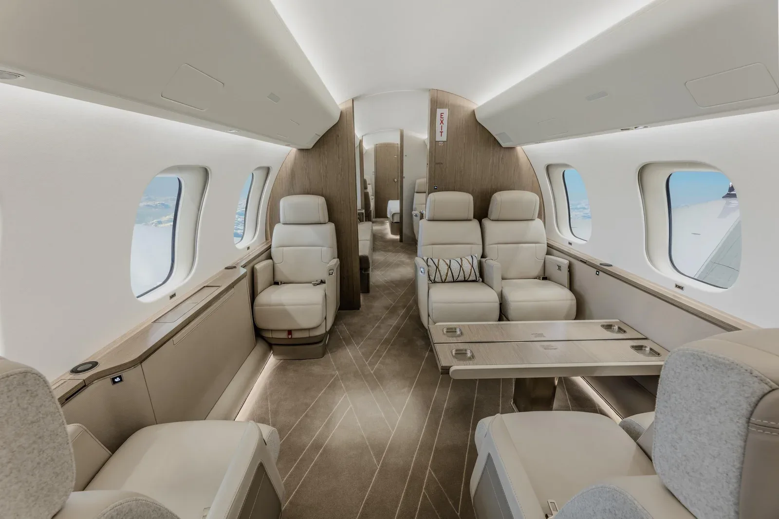 A view of the business jet cabin with light-colored seats, a wooden accent wall, and a table with cupholders.