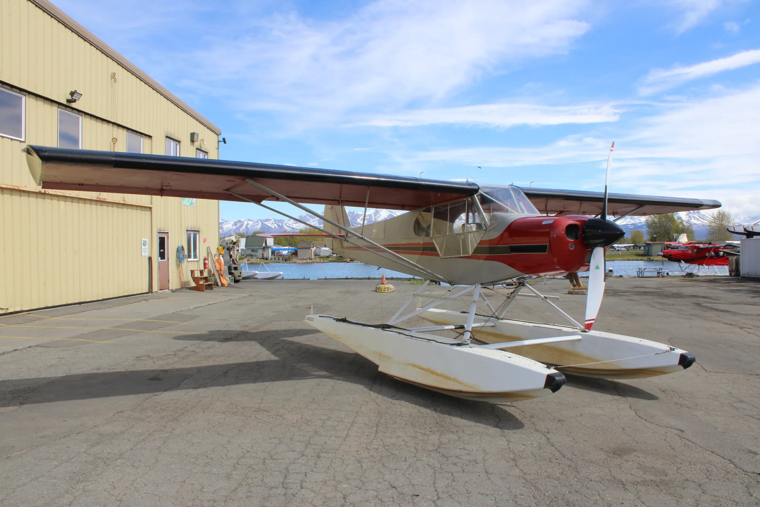 A red and silver float plane is parked in front of a hangar, angled view.