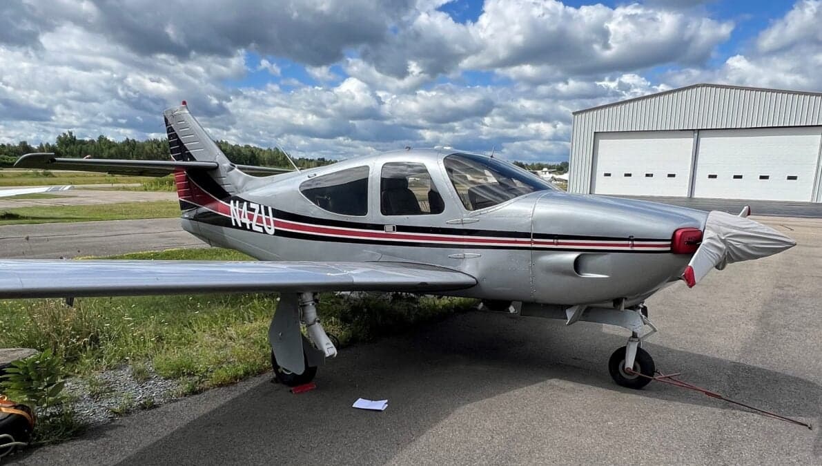 Side view of the N4ZU Mooney aircraft on the ground with a hangar in the background.