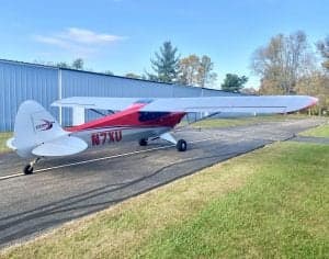 Side view of the red and silver Carbon Cub N7XU on the tarmac.