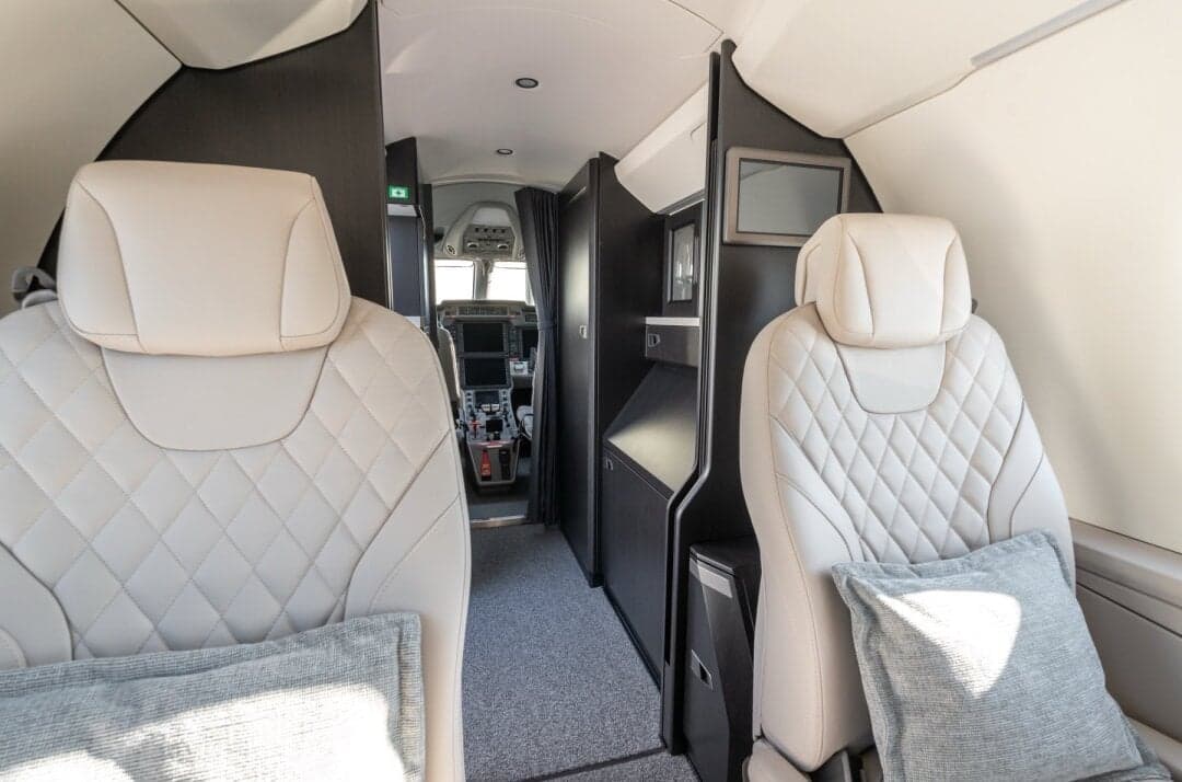 The private jet cabin interior with light-colored quilted seats, looking forward towards the cockpit.