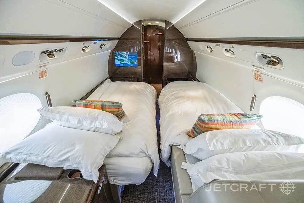 The aircraft cabin configured with two beds, complete with white bedding and colorful pillows.