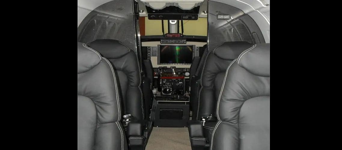 View of the interior cabin and cockpit of an aircraft with black leather seats.