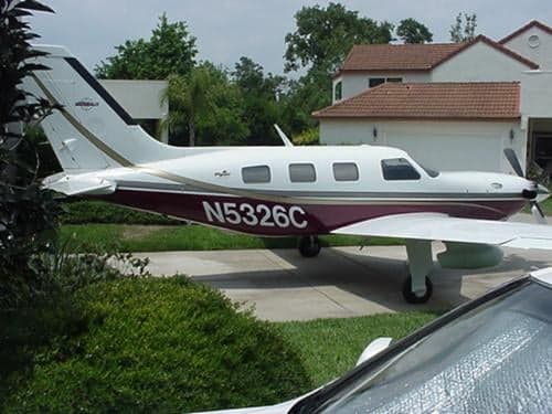 A maroon and white aircraft, N5326C, parked on a driveway with a car in the foreground.