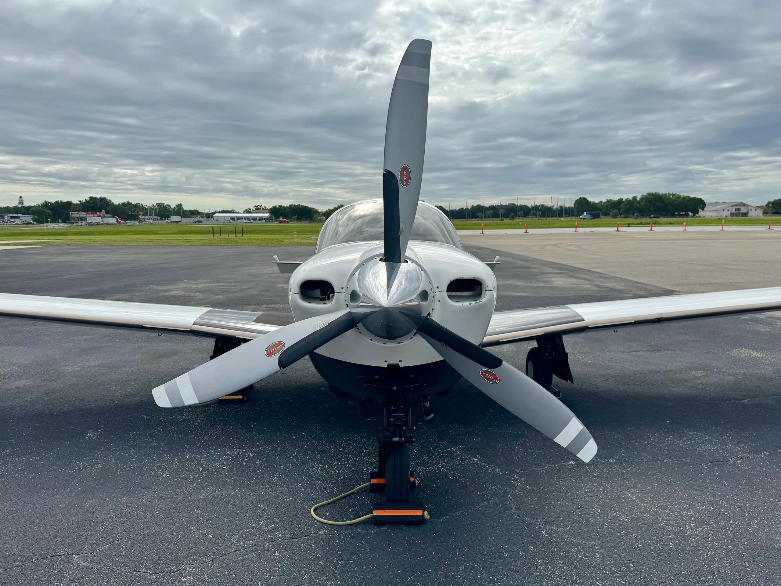 A head-on view of a Mooney aircraft, showcasing its propeller, spinner, and landing gear on an airfield.
