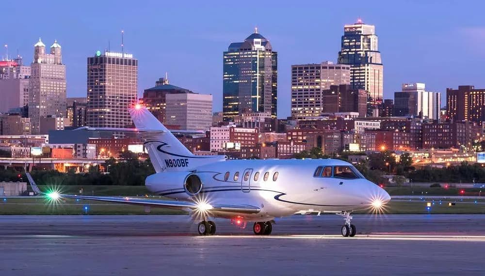 A white Hawker 800XP business jet, N900BF, on a runway at dusk with city lights in the background.