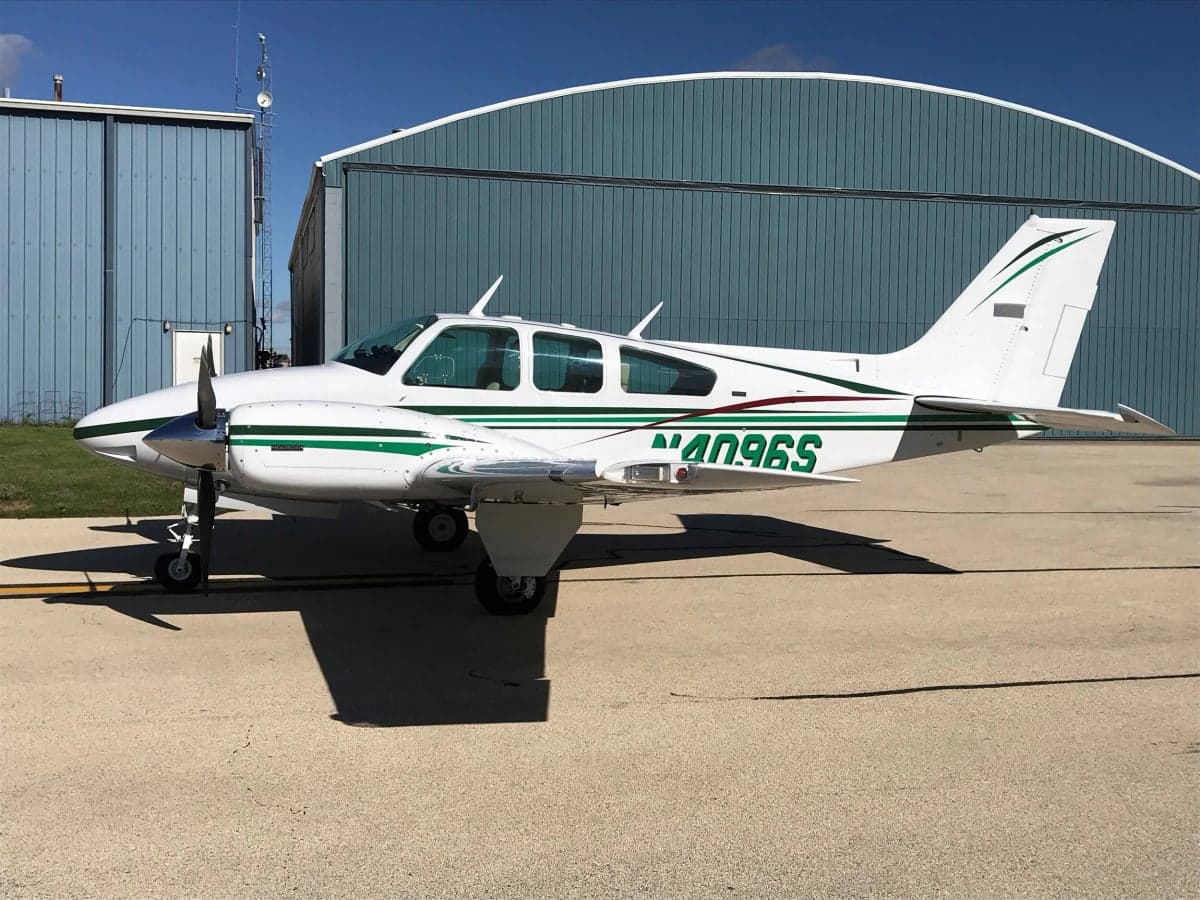 A white and green Beechcraft Bonanza is parked on the tarmac in front of a hangar.