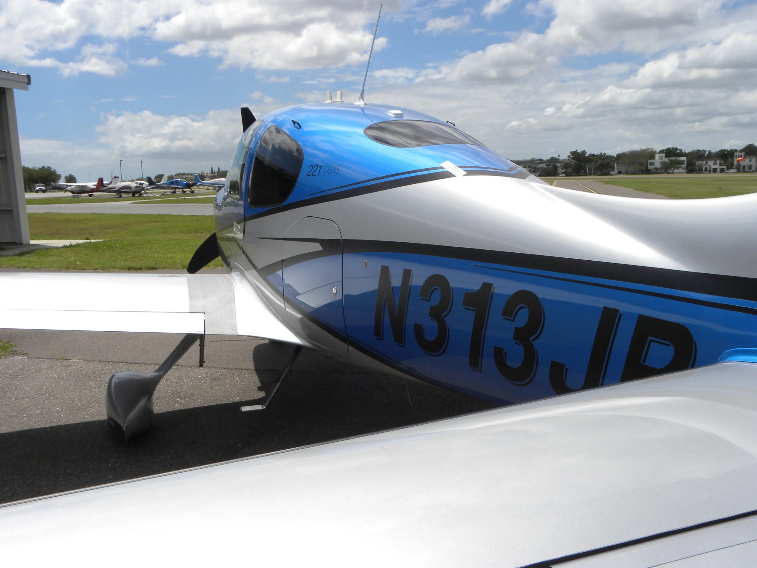 A rear-side view of a blue and silver Cirrus SR22T aircraft, N313JB, on an airfield.