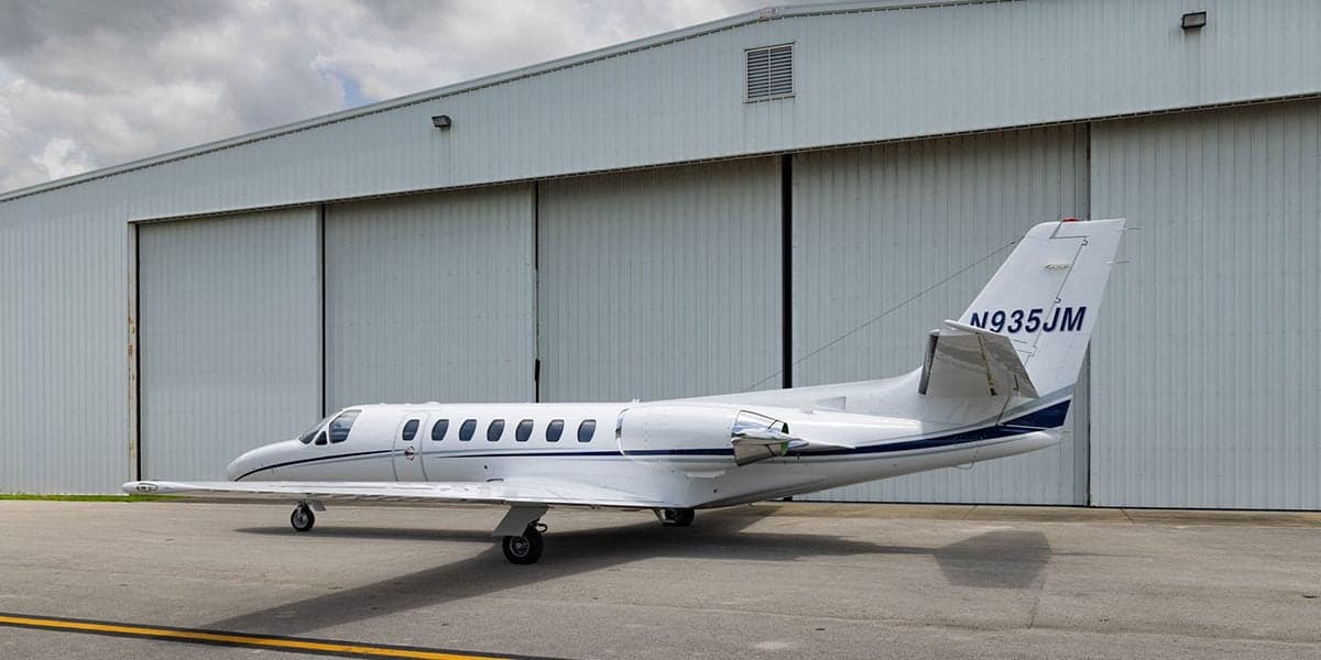 A Cessna Citation CJ3 aircraft is parked in front of a hangar, showing its side profile.