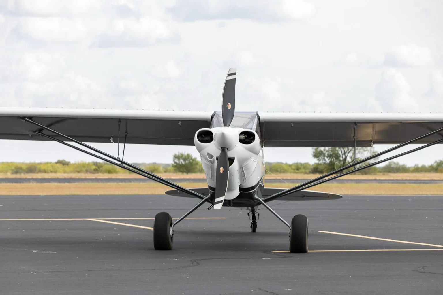 A head-on view of the white X-Cub aircraft with a black propeller, parked on an asphalt runway.