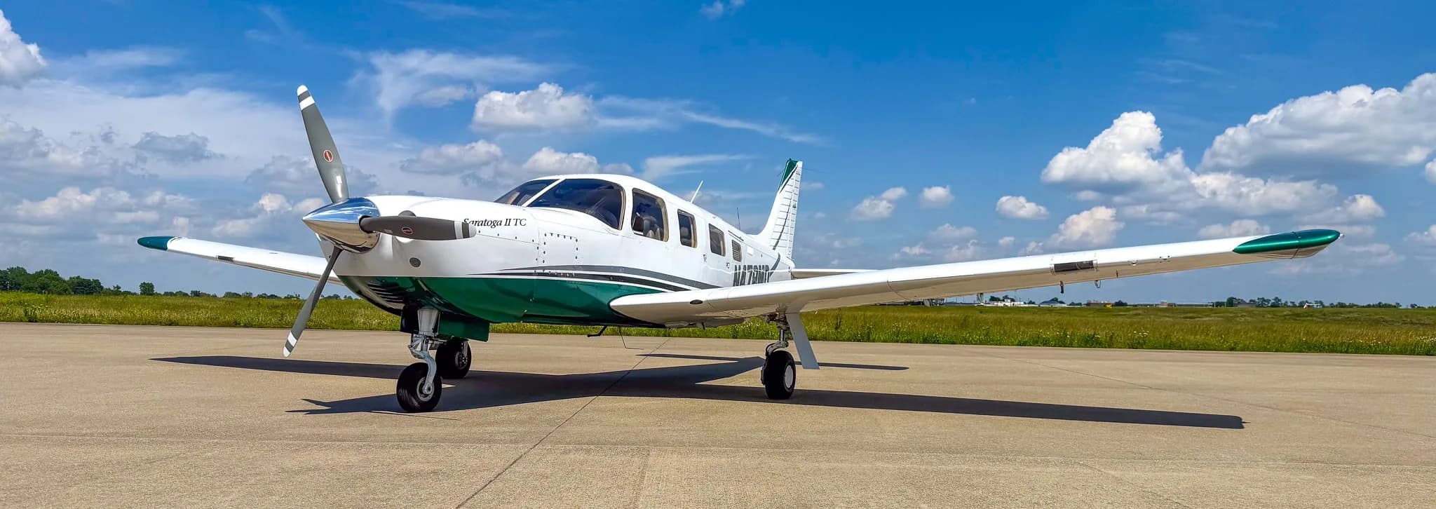 A white and green Piper Saratoga II TC aircraft (N478MD) parked on an airfield under a bright blue sky with scattered clouds.