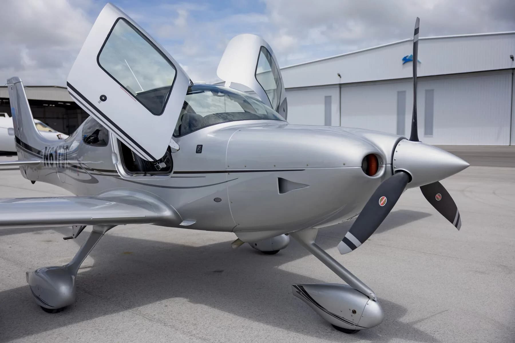 A close-up front-side view of the silver Cirrus SR22 aircraft with its gull-wing doors open and propeller.
