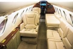 The aircraft's interior features cream-colored leather seats and wood trim.