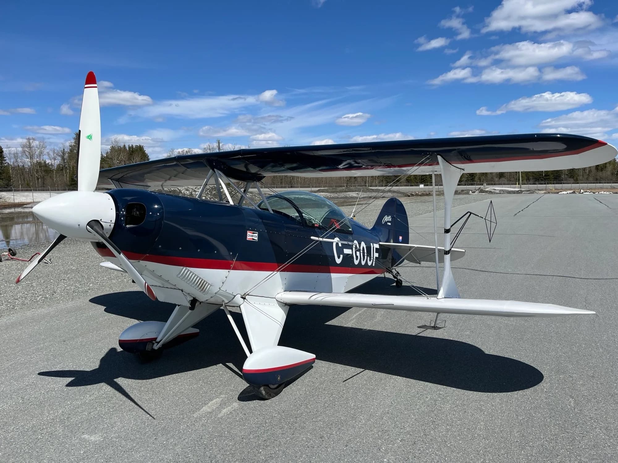 A dark blue, white, and red Pitts biplane with registration C-GOJF parked on an asphalt runway under a blue sky.