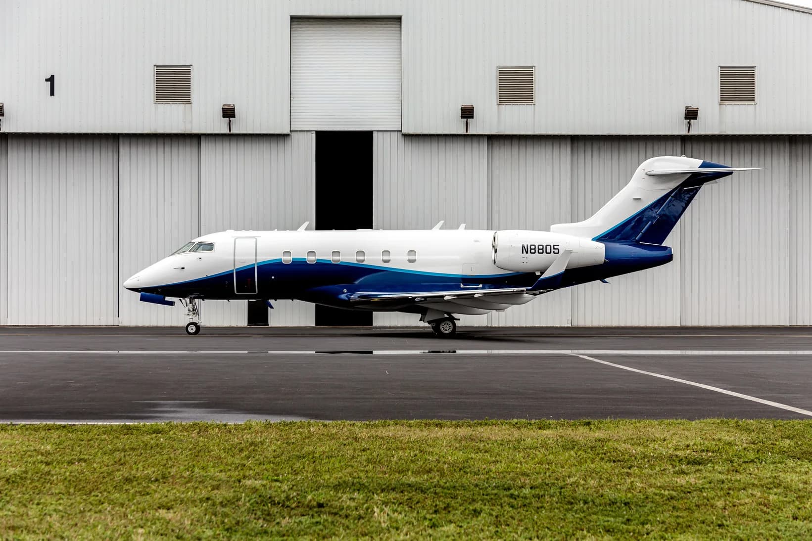 A white and blue private jet, registration N8805, parked on an tarmac in front of a hangar.