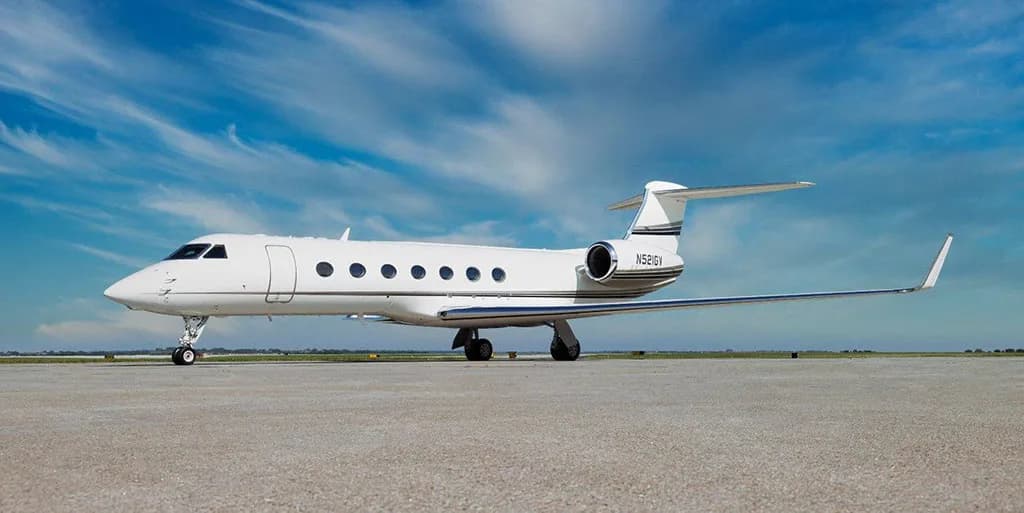 A white Gulfstream G550 business jet, tail number N521GV, parked on a tarmac under a blue sky.