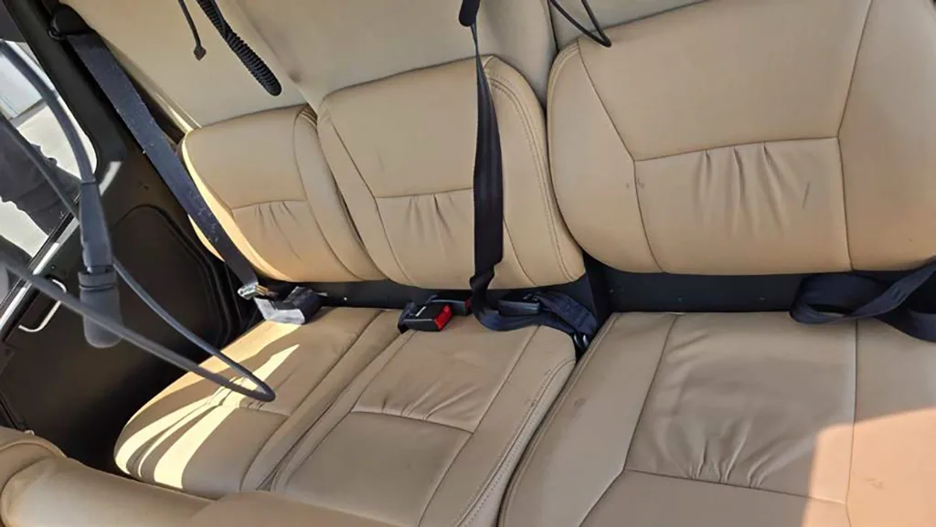 The tan leather rear cabin seats of a helicopter are shown with seatbelts fastened.