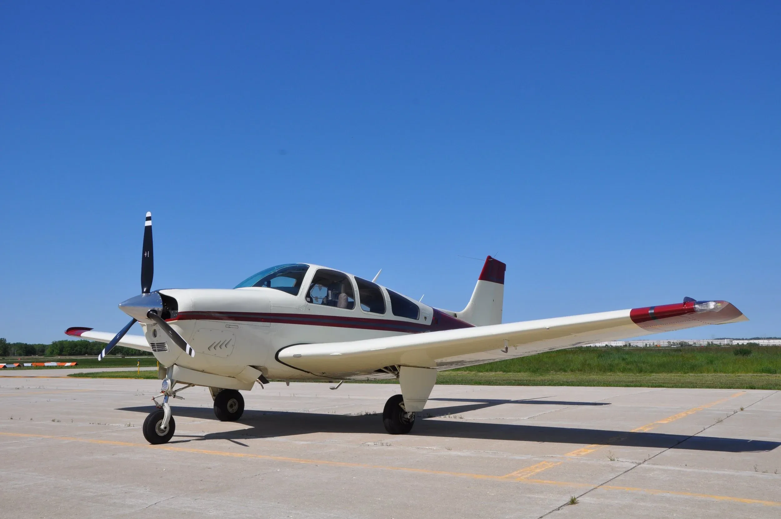 A white and red single-engine propeller aircraft parked on an airfield under a clear blue sky.