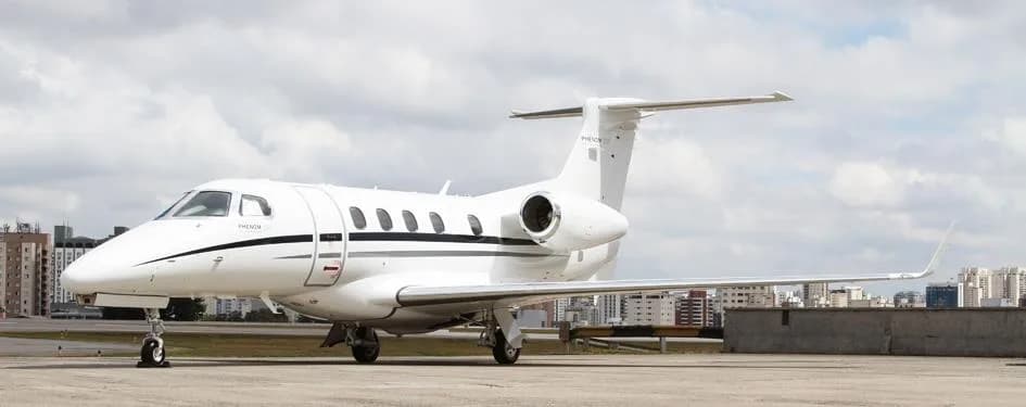 A Phenom 300E aircraft is parked on the tarmac with a city skyline in the background.