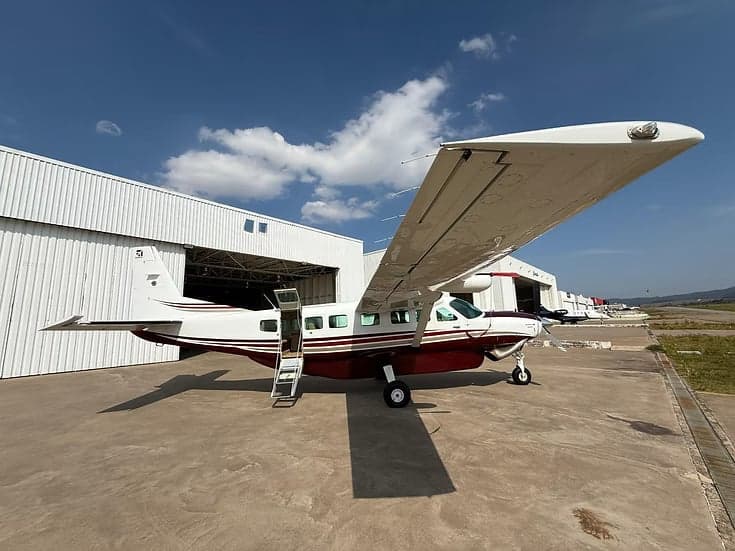 A maroon and white Cessna Caravan parked on the tarmac with the door open and a ladder extended.