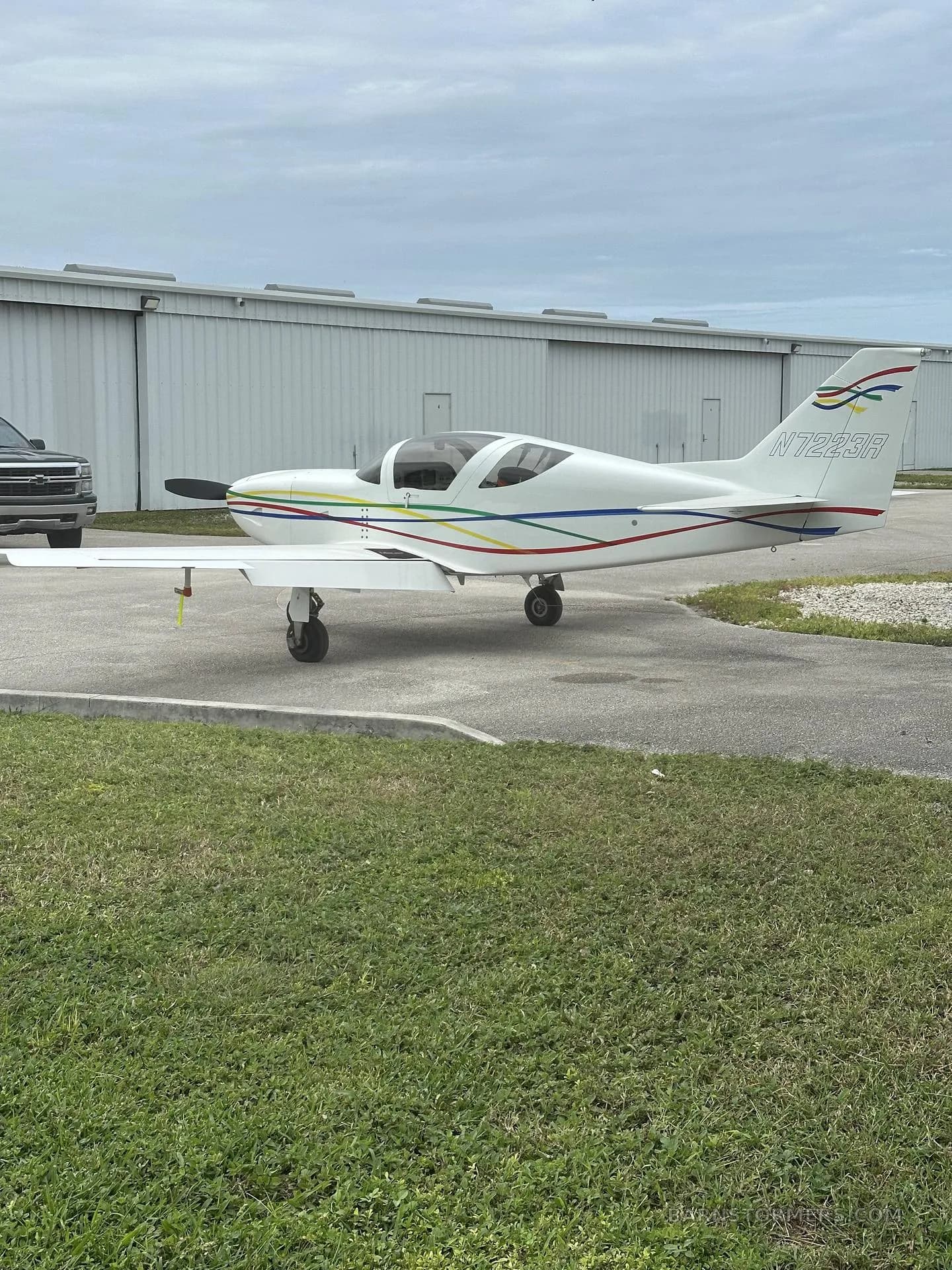 Side view of a white single-engine aircraft with colorful stripes along the fuselage and tail, parked on a tarmac.