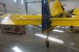 Tail section of a yellow and blue agricultural aircraft inside a hangar.
