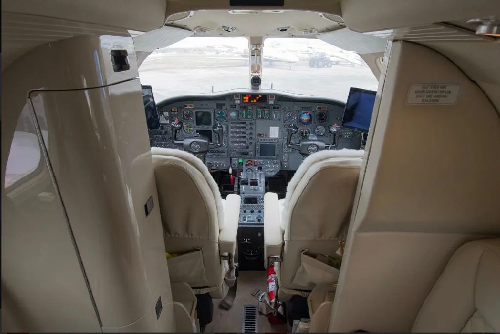 View into the cockpit of a private jet from the cabin, showing the instrument panel and two pilot seats.