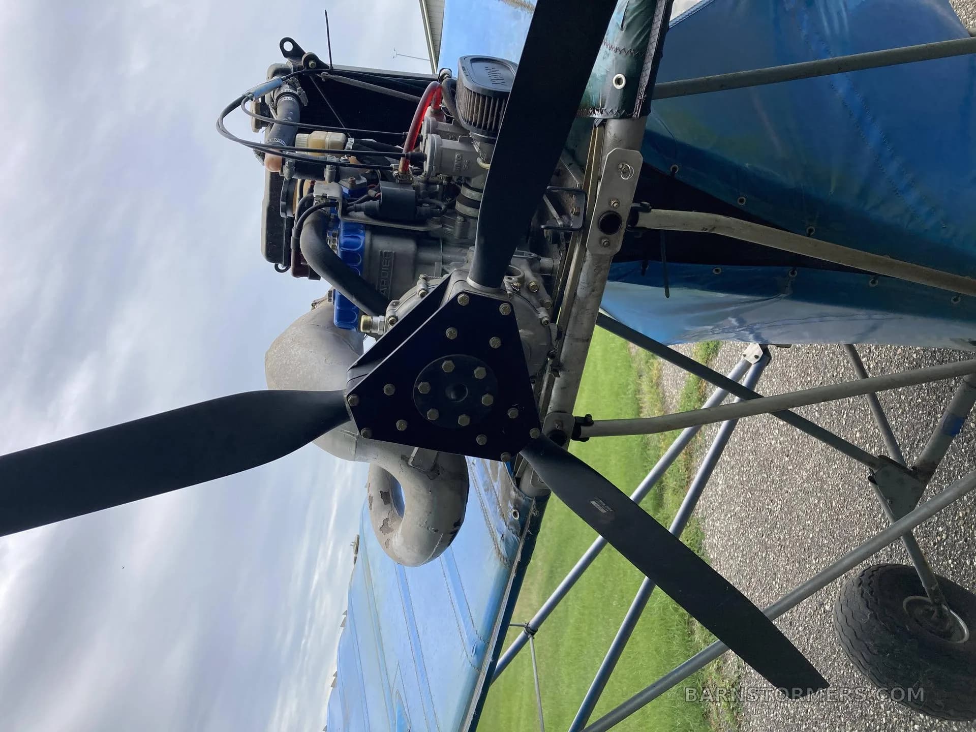 A close-up view of the three-blade propeller and exposed engine of a blue ultralight aircraft.