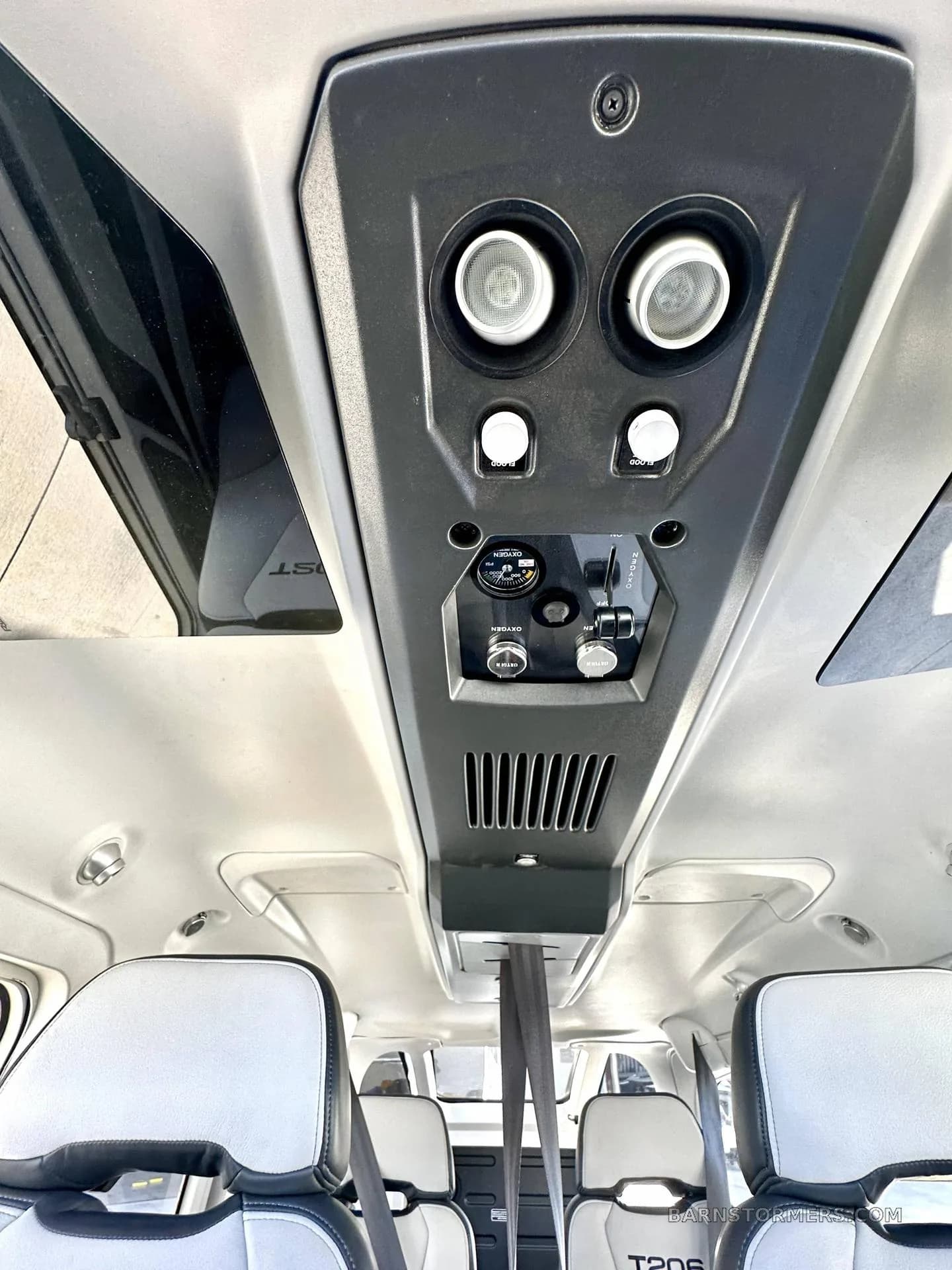 The overhead panel of a Cessna T206 cabin features air vents, lights, and oxygen controls, with light gray seats visible below.