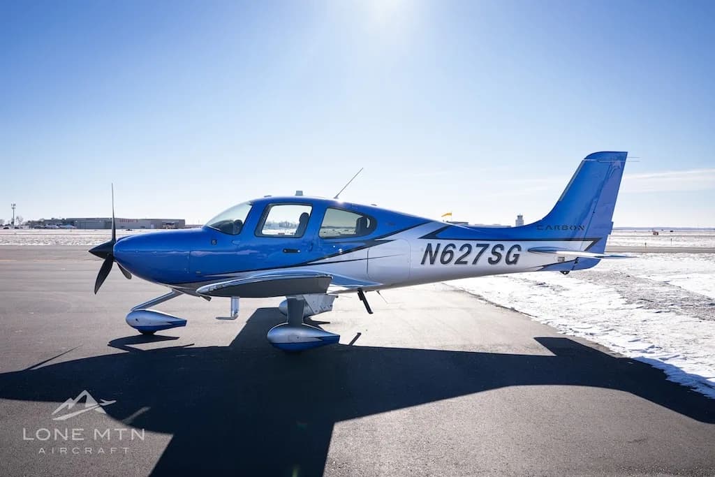 A side view of the blue and silver Cirrus SR22 aircraft (N627SG) on a snowy airfield.