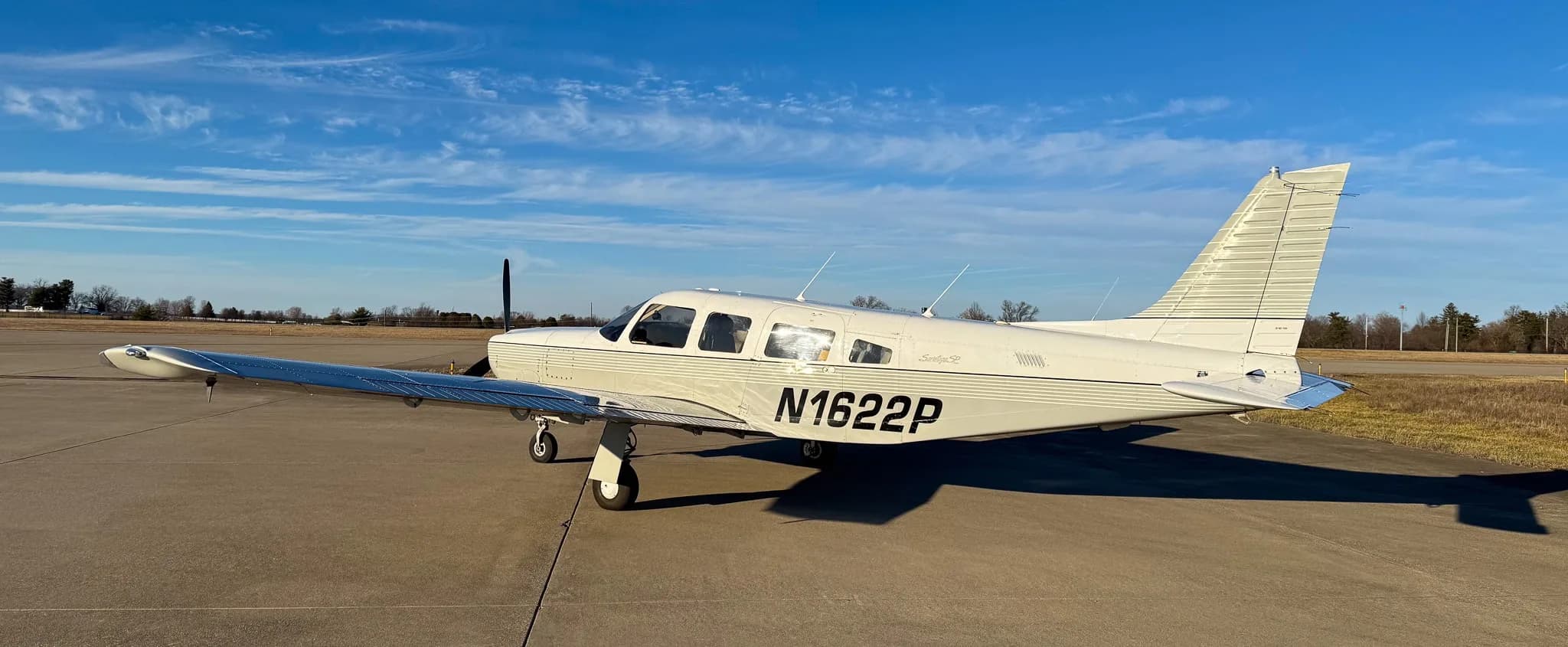 A three-quarter rear view of a white Piper Saratoga SP (N1622P) with grey stripes on an airfield.