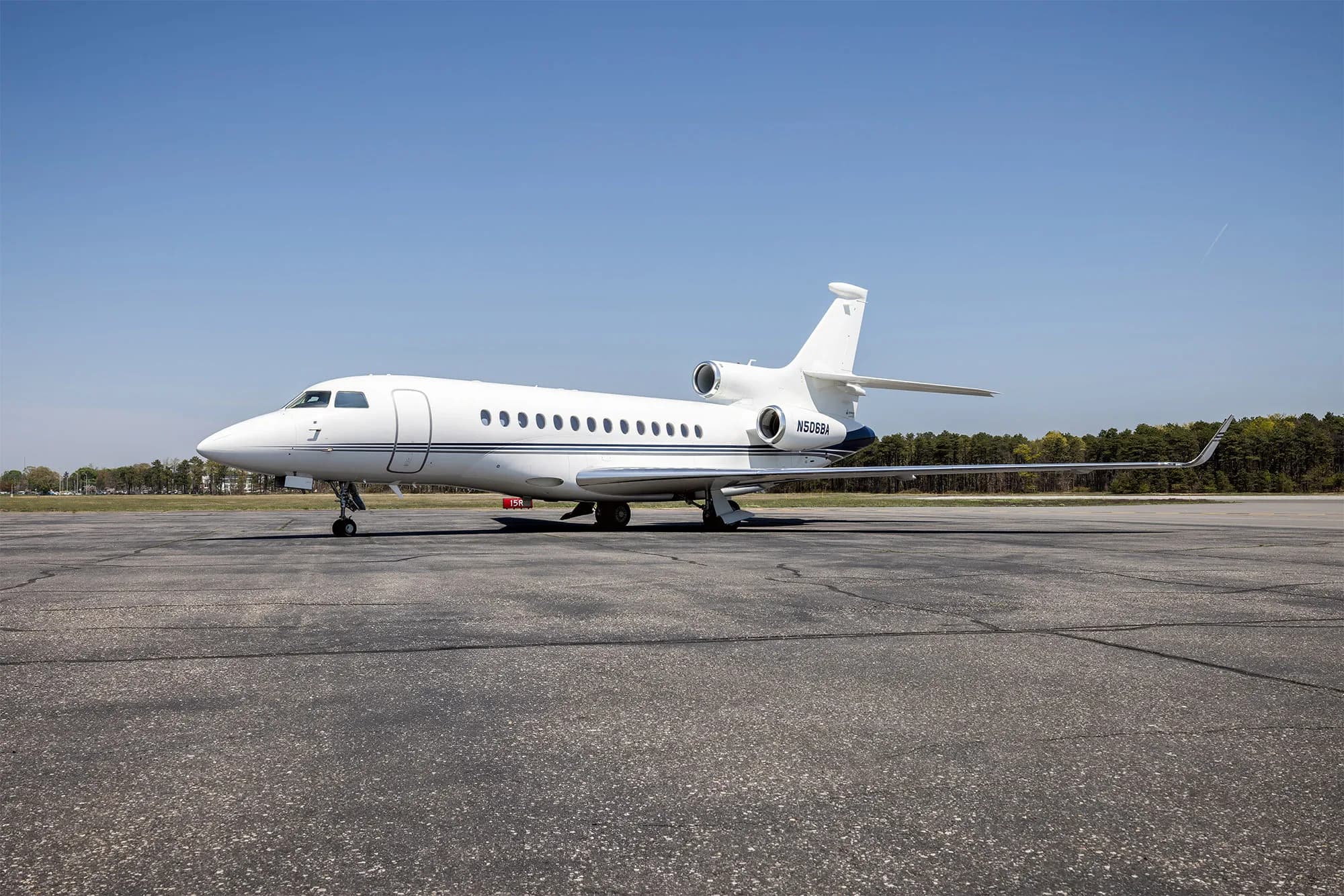 A white Dassault Falcon 50 business jet with blue accents on the tail, parked on an asphalt tarmac under a clear blue sky.