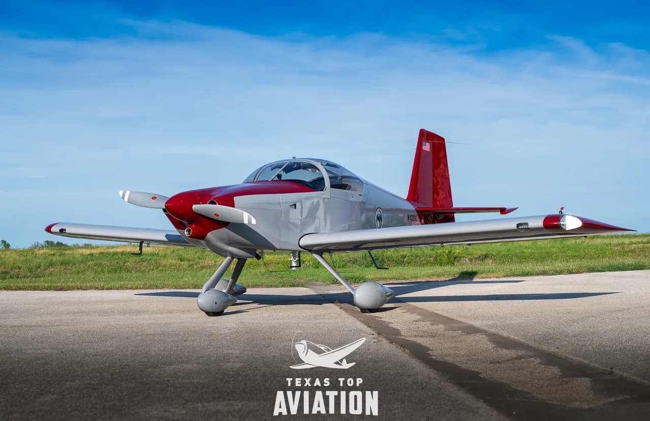 A gray and red single-engine aircraft, N1359L, with its tail number visible, parked on a tarmac.