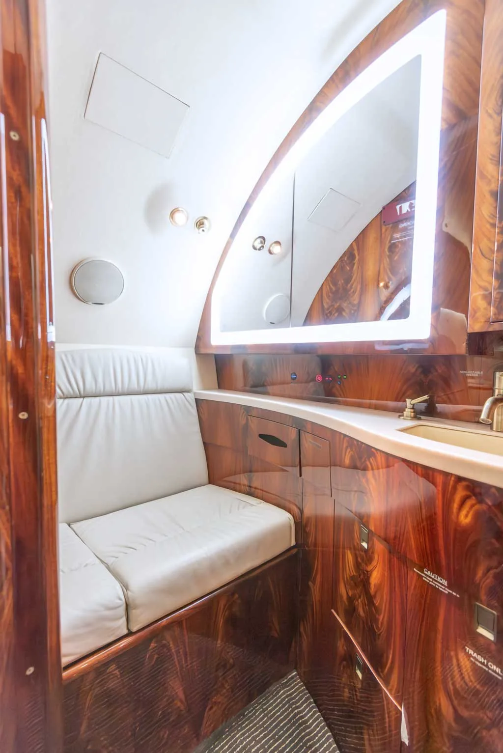 A private jet lavatory or lounge area with a lighted mirror, sink, and white leather bench seat.