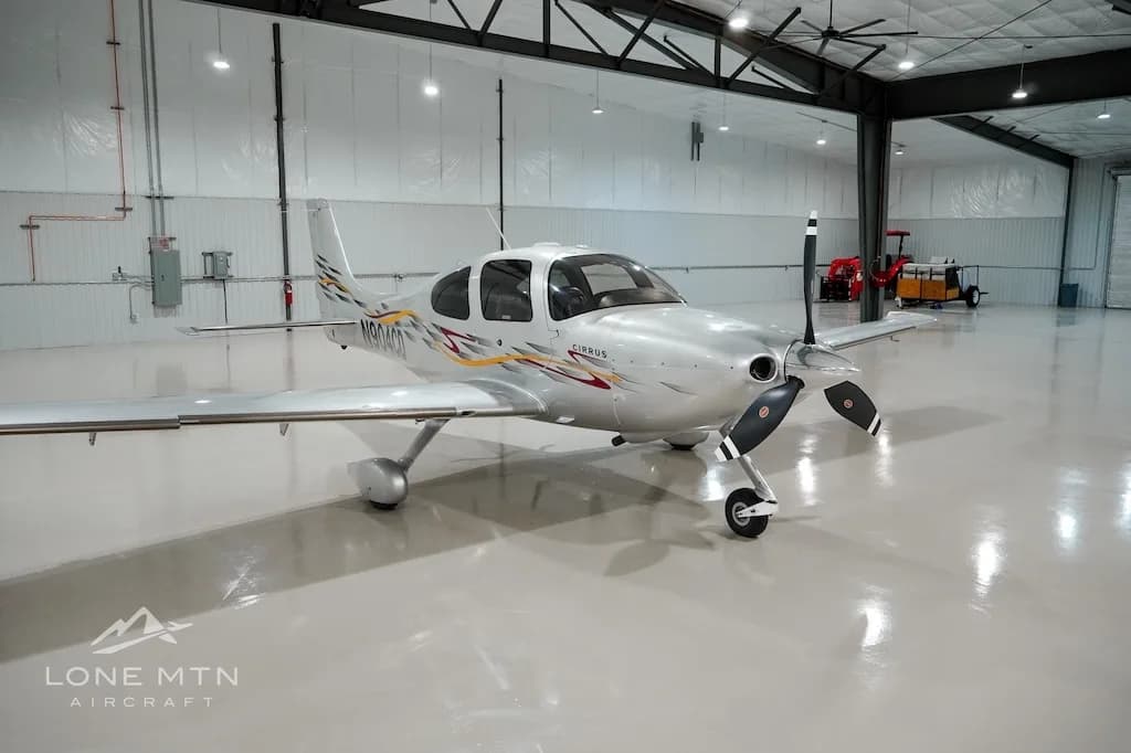 A silver Cirrus aircraft with red and yellow accent stripes, registration N904CD, parked in a hangar.
