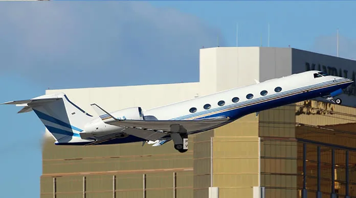 A white and blue jet aircraft takes off in front of a building.