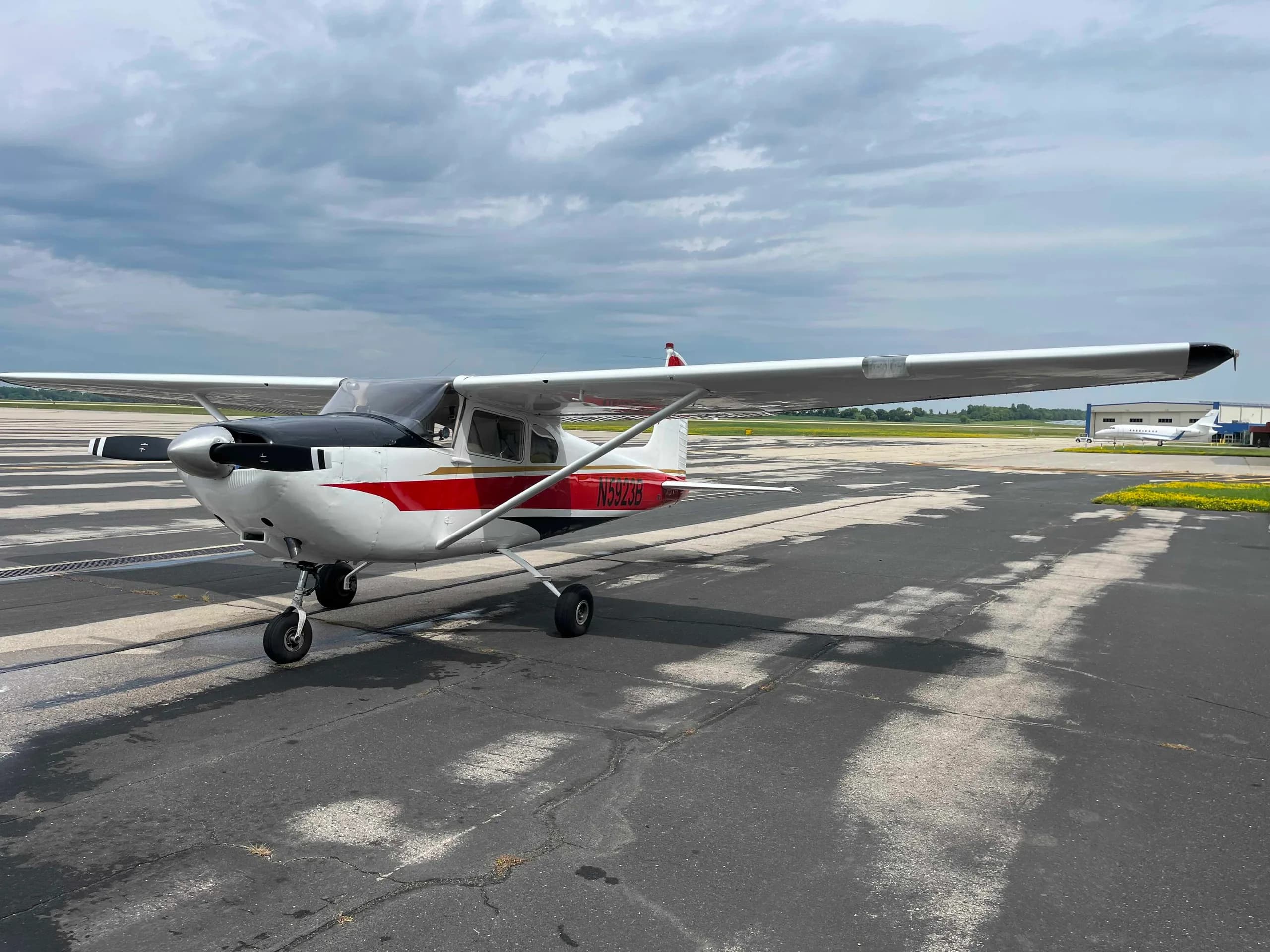 A three-quarter front view of a white Cessna 182 aircraft with red and black stripes and registration N5923B, parked on an airport taxiway.