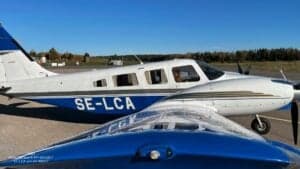 A Piper Seneca III PA-34-220T aircraft with registration SE-LCA on the tarmac, with another aircraft in the foreground.