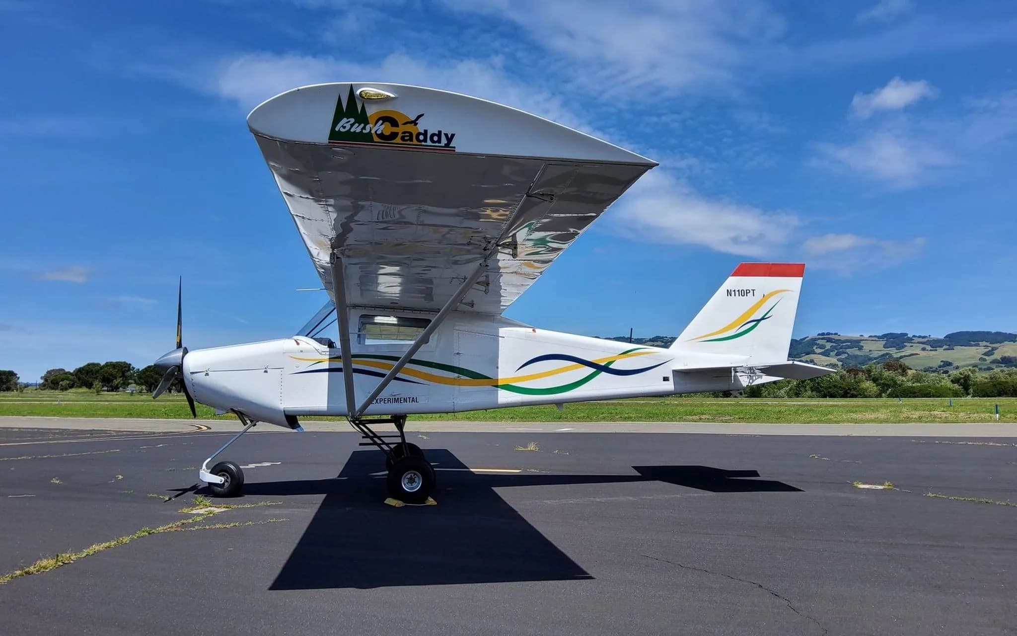 A white BushCaddy aircraft with "N110PT" on the tail and "BushCaddy" logo on the wing, parked on a sunny tarmac.
