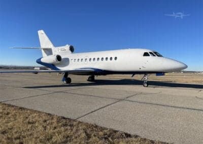 A white and blue Dassault Falcon 900EX, registration C-GEOS, parked on the tarmac.