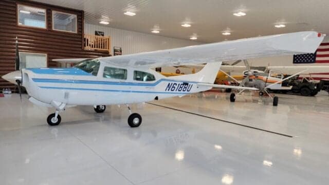 Close up of the front of a Cessna Centurion aircraft with a blue and white paint scheme inside a hangar.