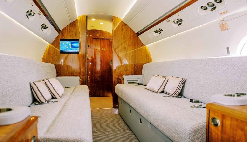 The aircraft's interior features white leather seats and wood trim.