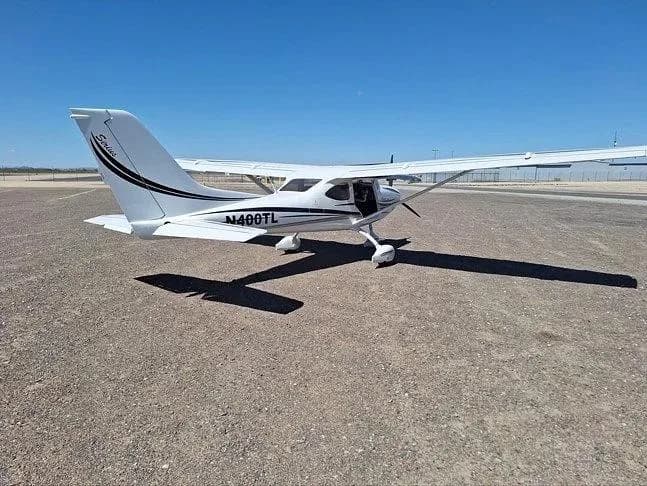 A rear three-quarter view of a white Sirius LightSport aircraft with black and grey stripes, registration N400TL, parked on an airfield.