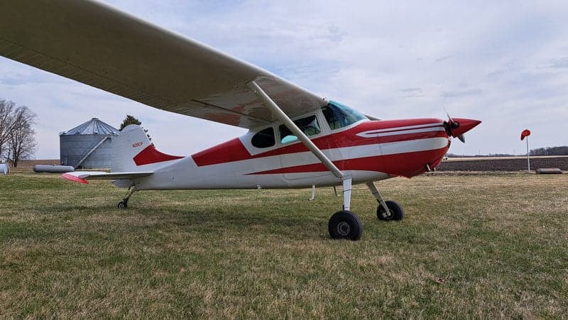 A side view of the red and white Cessna on a grassy field.