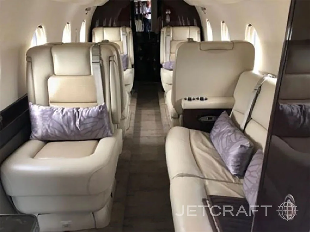 The luxurious interior cabin of a private jet with cream leather seats and purple pillows.