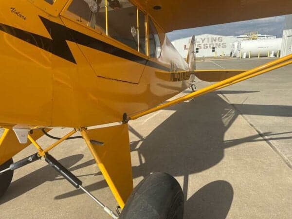 Close-up side view of the fuselage of a yellow Legend Cub aircraft with registration N267RJ, showing the landing gear.