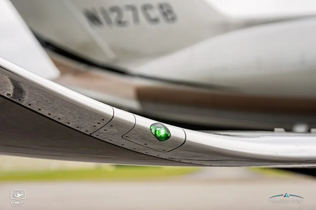 A close-up view of the wingtip of a business jet, showing a green navigation light and the N127CB registration in the background.